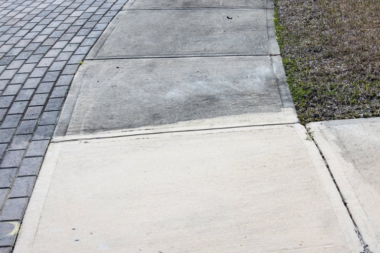 Partially cleaned and partially dirty cement sidewalk in front of a home after some of it has been pressure washed and some has not
