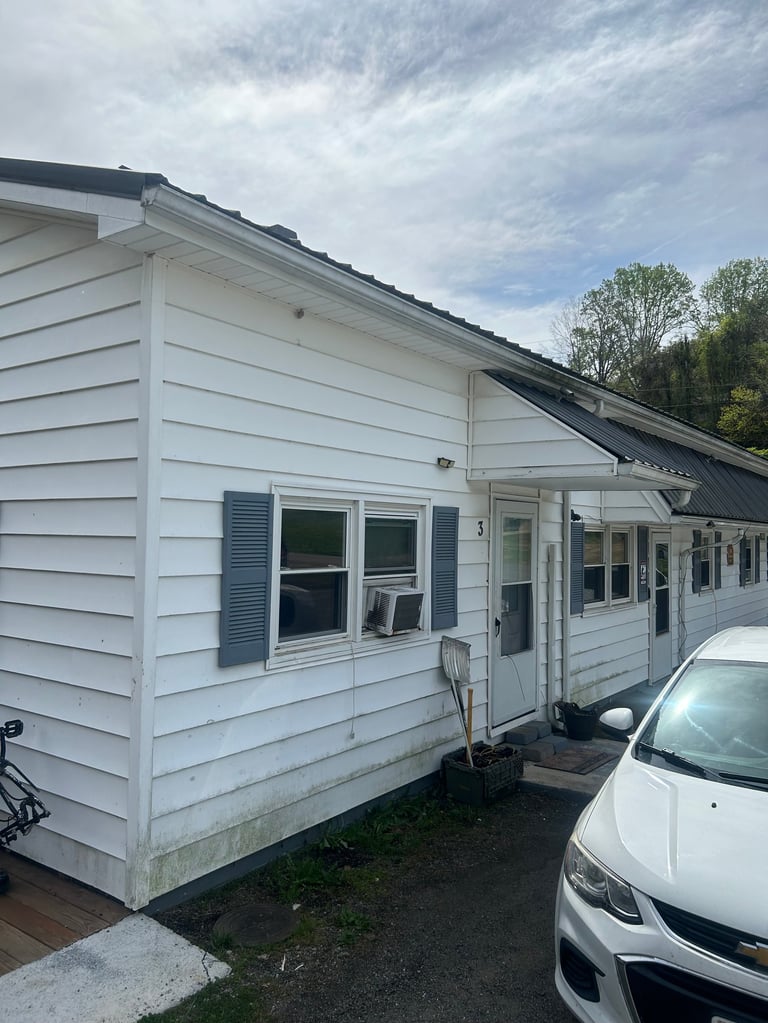 White mobile home with dark roof and blue shutters parked next to white car on cloudy day