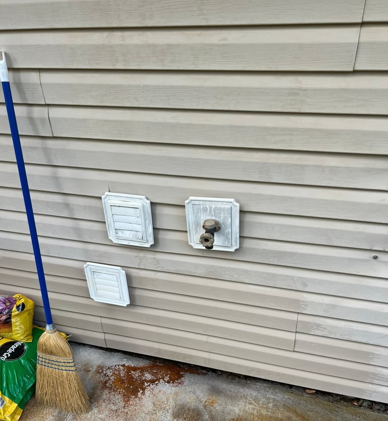 Beige vinyl siding exterior wall with three white electrical outlet covers and a blue pole with cleaning supplies at ground level