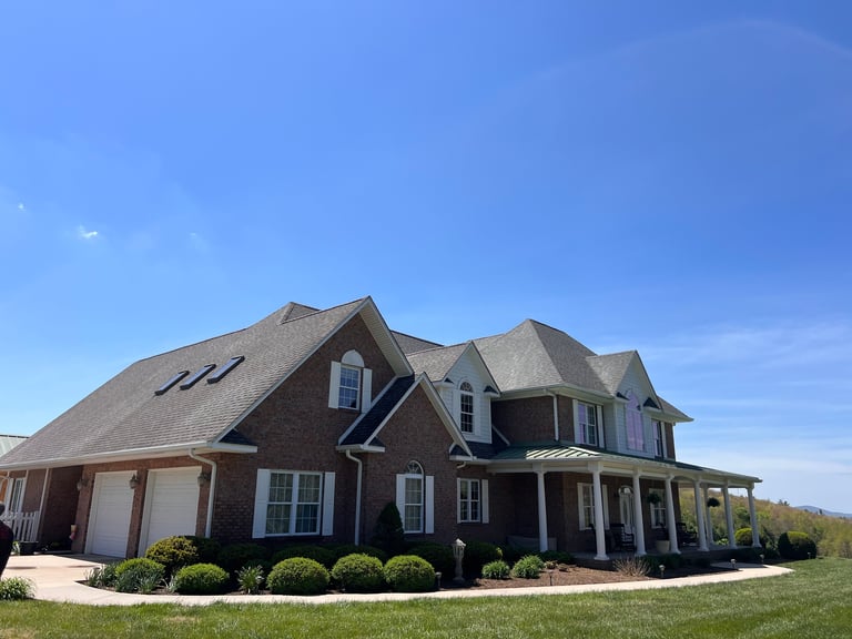 Large brick two-story house with peaked roof and attached garage under clear blue sky on sunny day