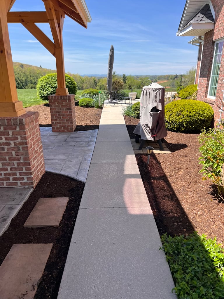 Patio walkway leading from brick house to landscaped yard with pergola green trees and scenic hillside view under blue sky