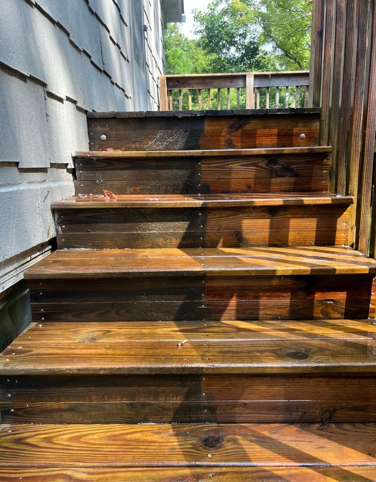 Wooden deck stairs with shadow patterns cast across the steps, adjacent to a metal railing and gray building