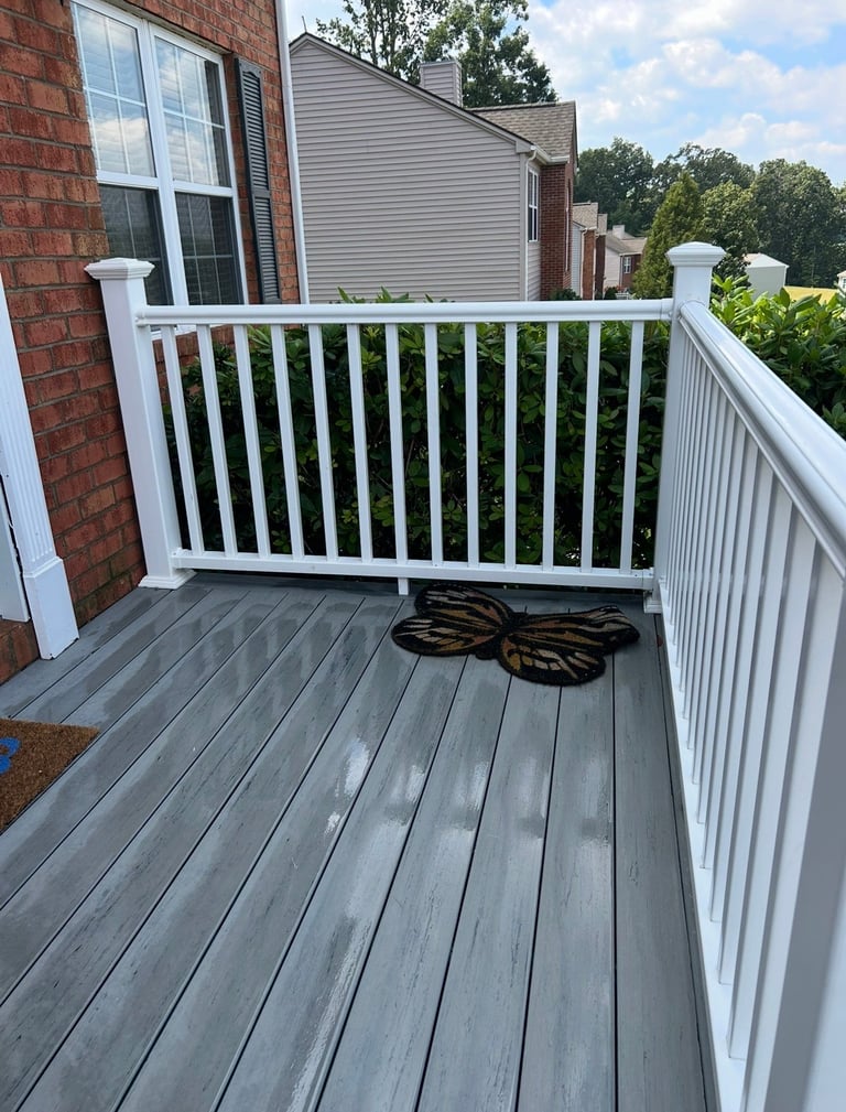 Gray composite deck with white railings attached to brick house, coiled hose on deck, overlooking wooded neighborhood