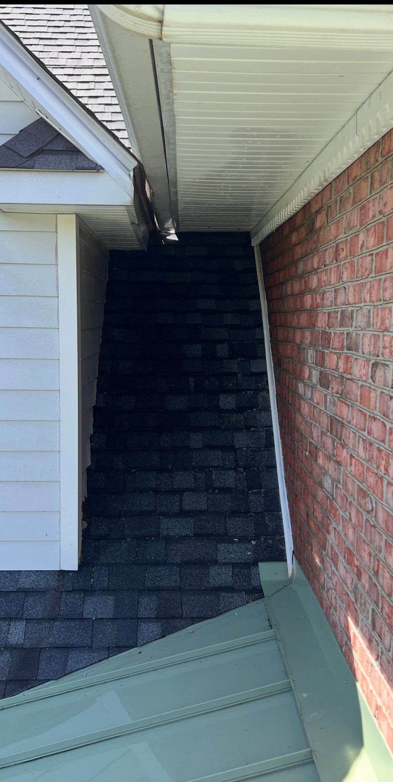 Dark asphalt shingle roof viewed from garage entrance between white garage door and red brick wall