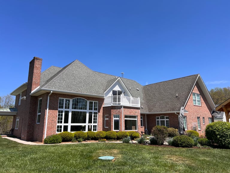 Two-story brick and stone residential home with gray roof chimney and manicured lawn under clear blue sky