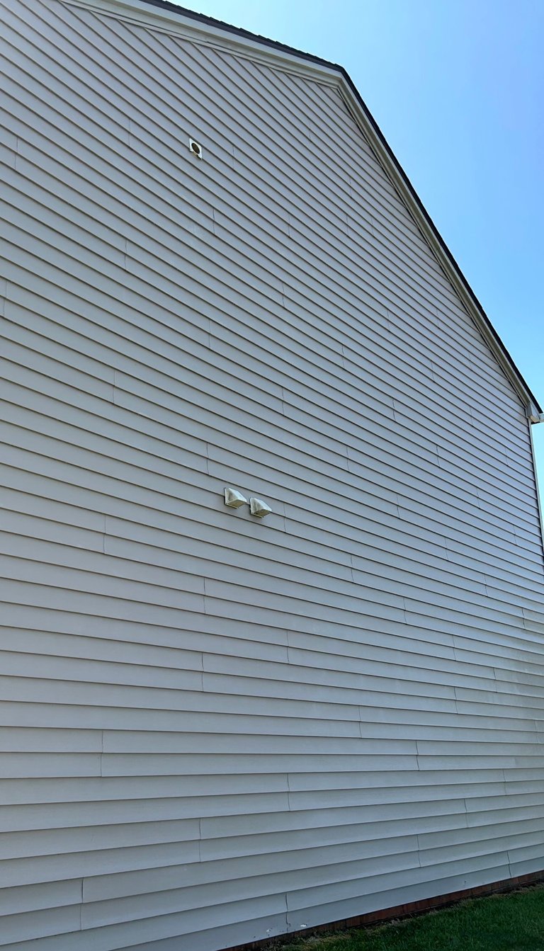 Light gray horizontal vinyl siding on a residential building wall sloping upward against a clear blue sky