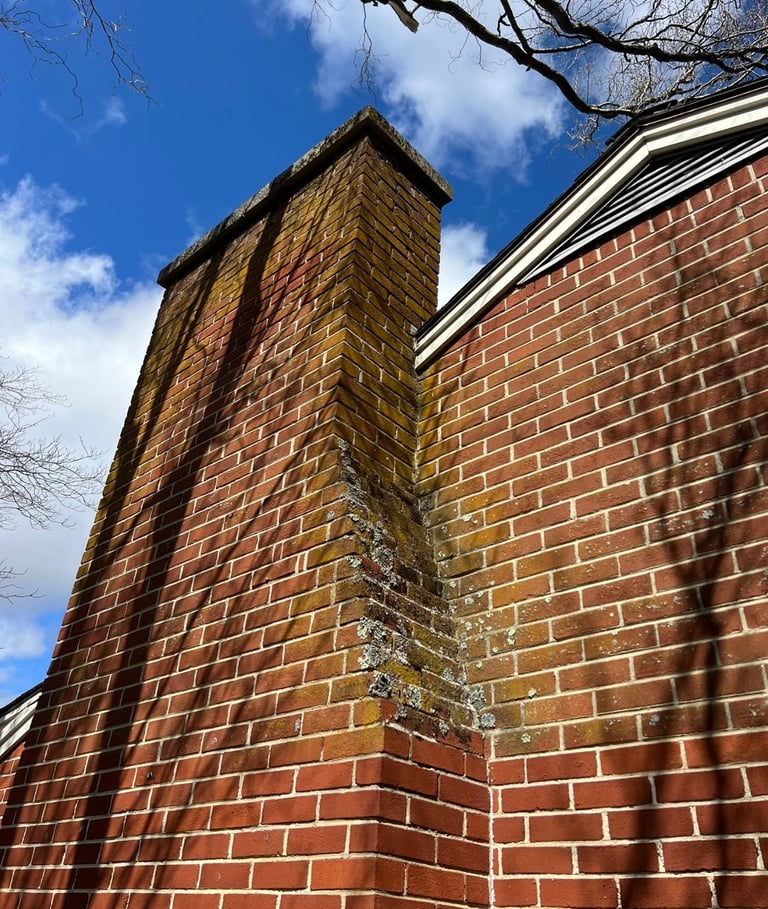 Tall red brick chimney rising from brick building against blue sky with bare tree branches visible