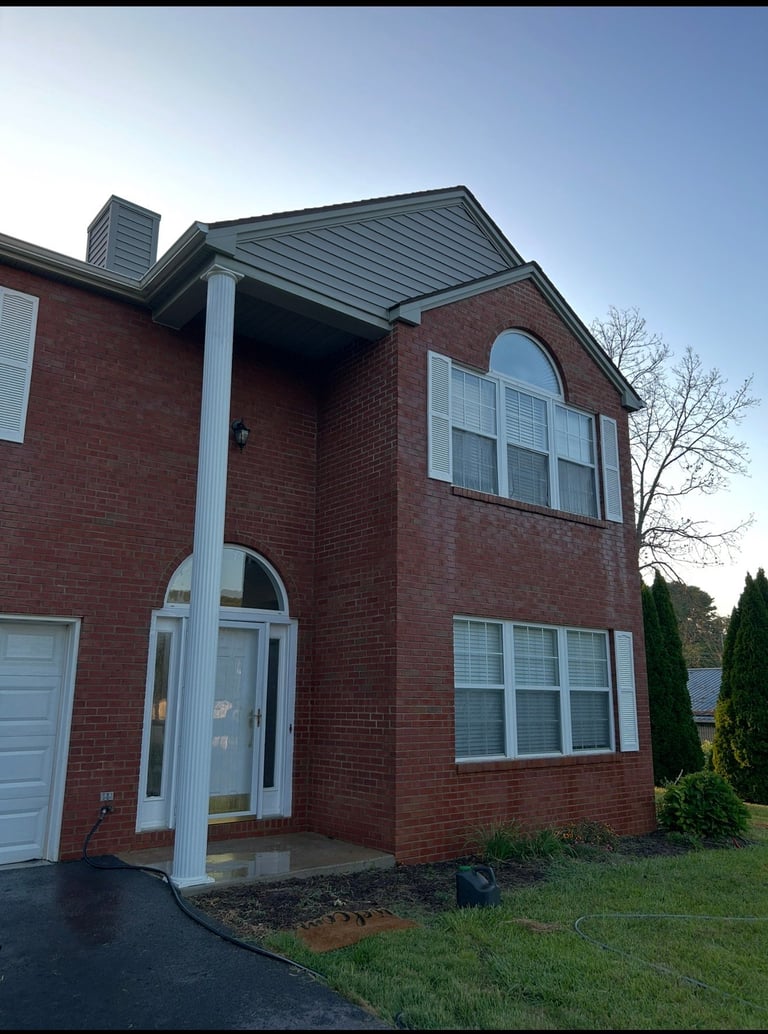Two-story red brick house with dark roof, white trim, arched entryway, and large windows, with driveway and landscaping
