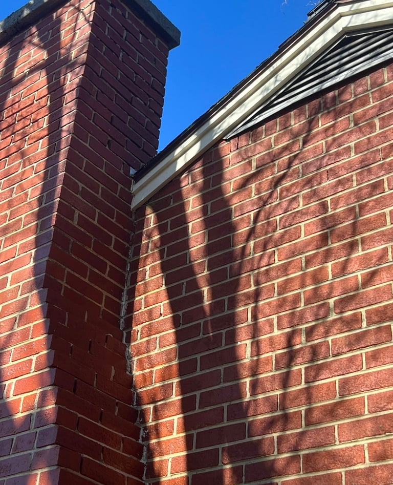Brick building corner with chimney casting shadow against red brick wall under clear blue sky