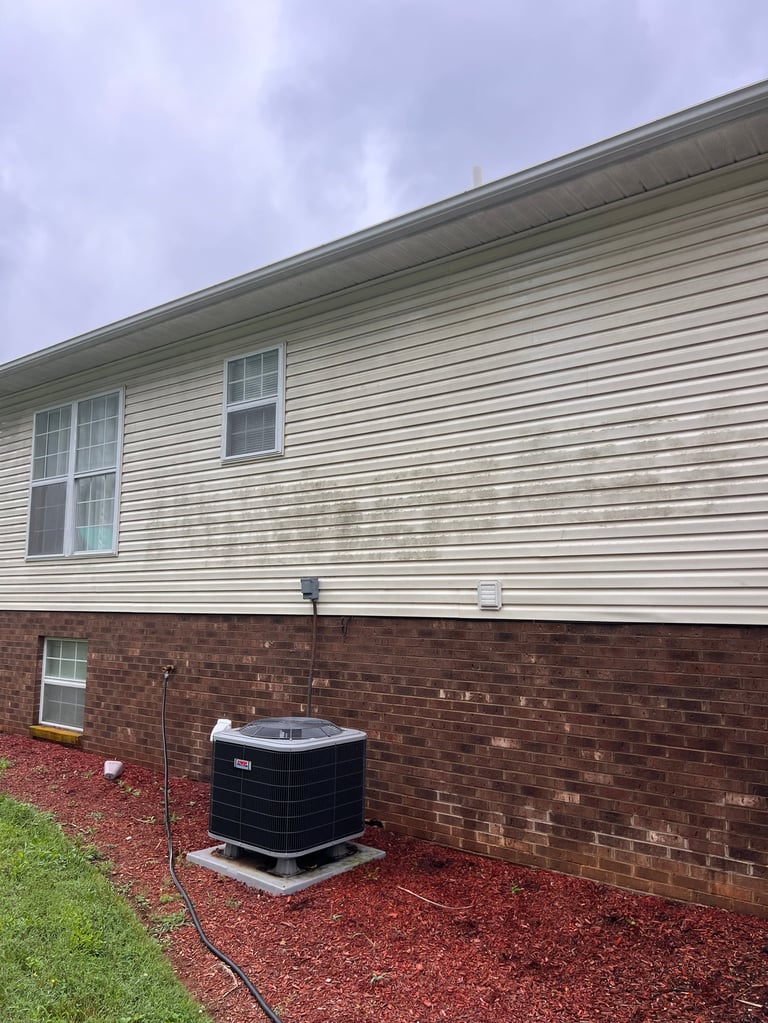 Outdoor HVAC unit positioned on red mulch against brick and vinyl siding of residential home with lawn