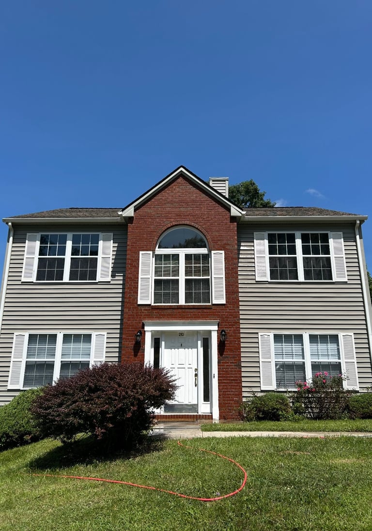 Two-story brick and siding house with white trim, arched window, and manicured lawn under clear blue sky
